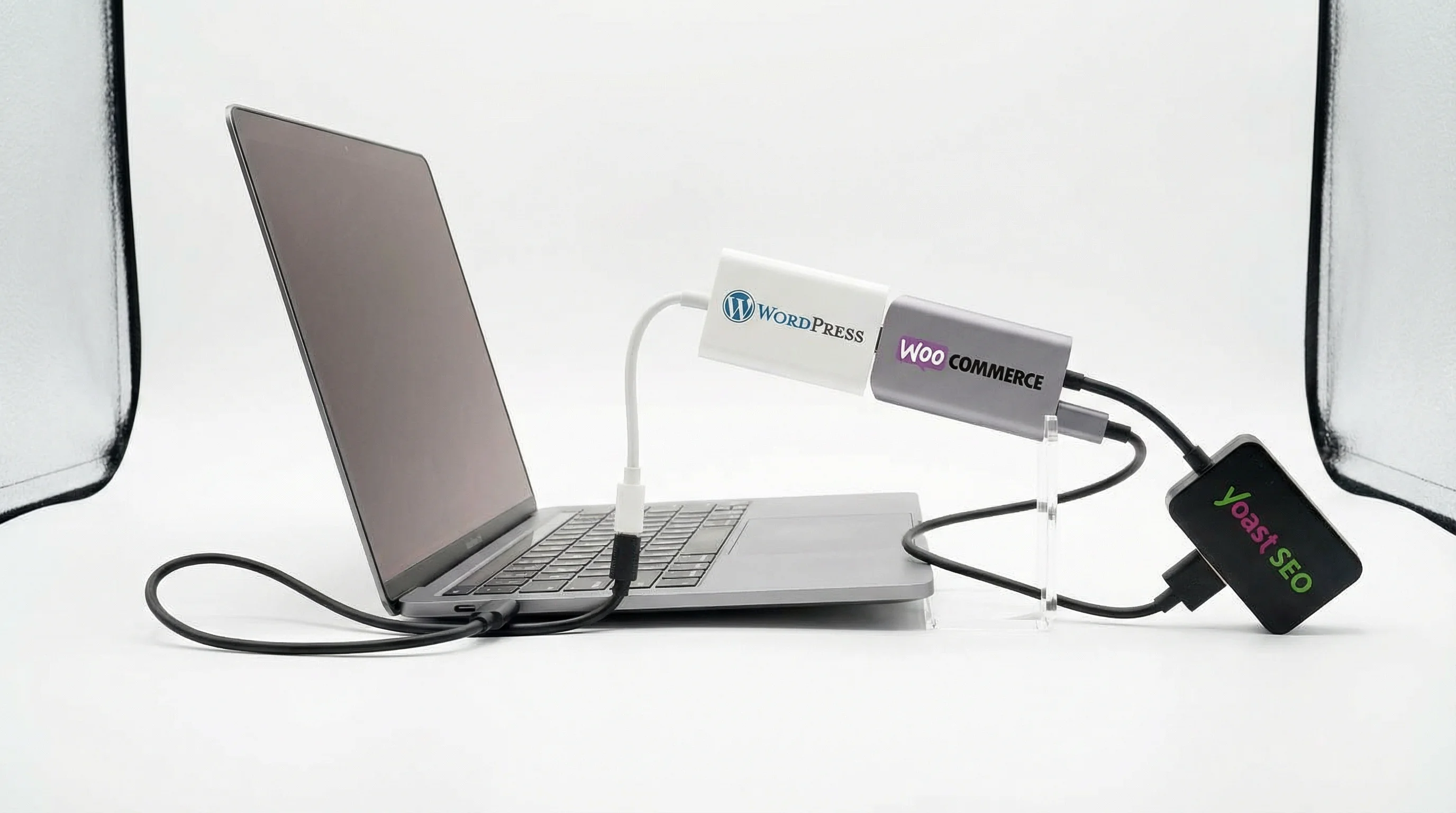A humorous photo showing three USB dongles daisy-chained together sticking out of a laptop, labelled WordPress, WooCommerce, and Yoast SEO